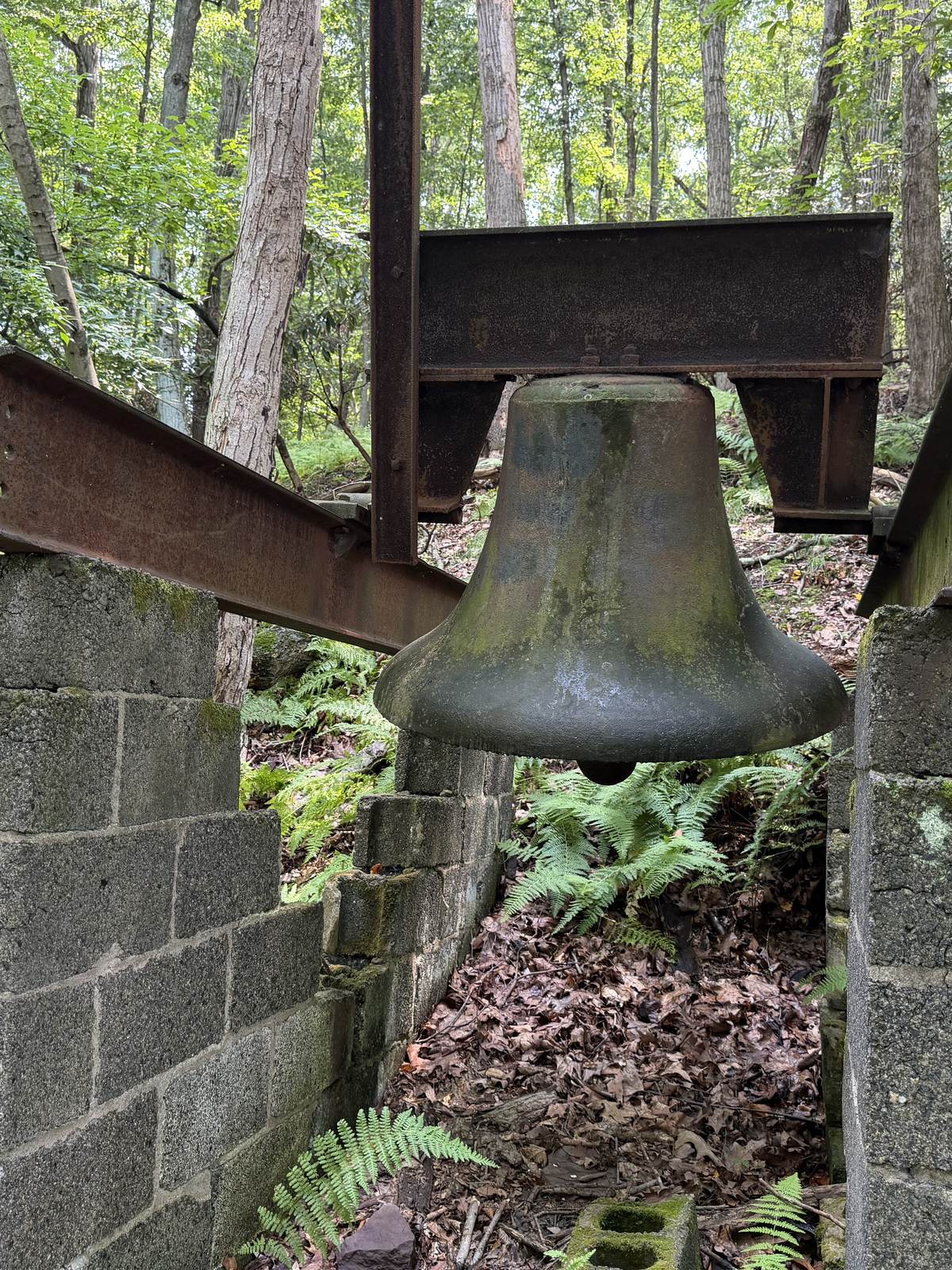 The church bell, green with age, hanging from a steel frame in the woods